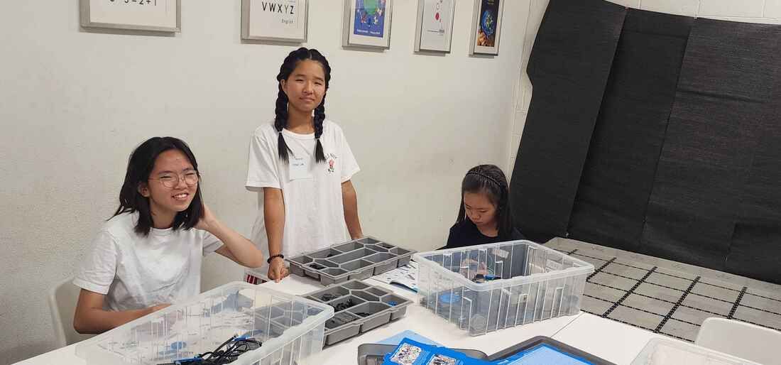 Three volunteers smiling at a table with camp materials